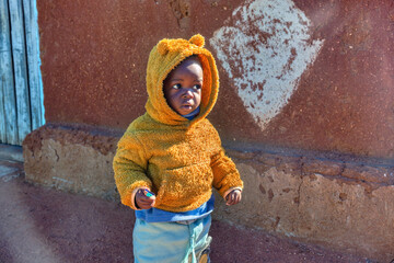africa village, single african child toddler with a hoodie, in the township , cold day, standing...