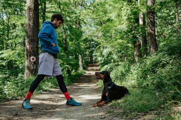 Young man training doberman pinscher on hiking trail in forest