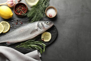 Fresh raw seabass fish with spices on grey table, flat lay and space for text. Seafood delicacies