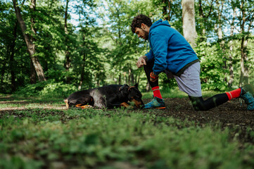 Runner kneeling next to doberman pinscher in forest