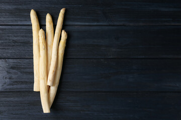 Raw white asparagus spears on black wooden table, flat lay. Space for text