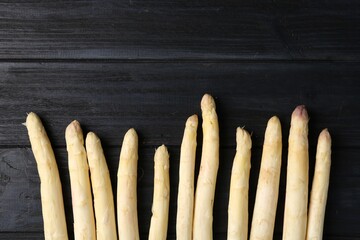 Raw white asparagus spears on black wooden table, flat lay. Space for text