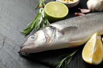 Fresh raw seabass with spices on black table, closeup. Fish and seafood delicacies