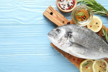 Fresh raw dourade fish with spices on blue wooden table, flat lay and space for text. Seafood...