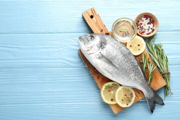 Fresh raw dourade fish with spices on blue wooden table, flat lay and space for text. Seafood...