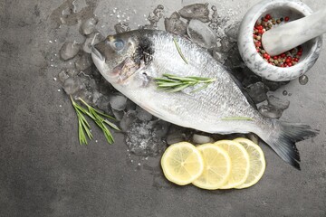 Fresh raw dourade fish, ice, lemon slices and rosemary on grey table, flat lay. Organic seafood