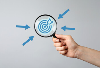 Woman holding magnifying glass with target inside against grey background, closeup. Arrows pointing at magnifier