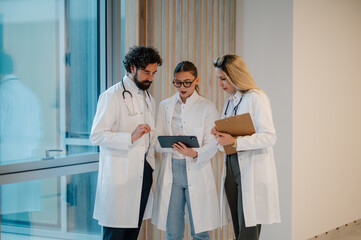 Medical team examining patient data on tablet in hospital corridor
