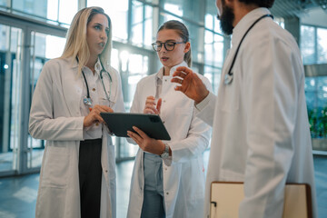 Medical team discussing patient data on tablet in hospital hallway