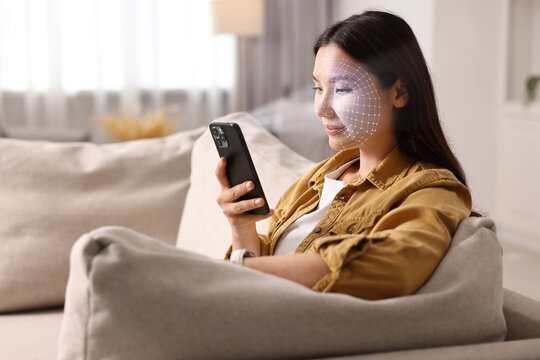 Woman unlocking her smartphone with facial recognition app at home. Biometric verification