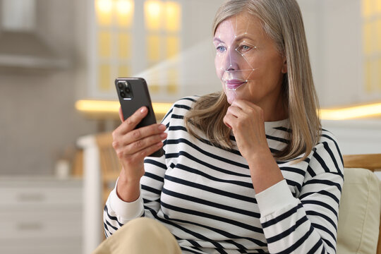 Woman unlocking her smartphone with facial scanner in kitchen. Biometric verification