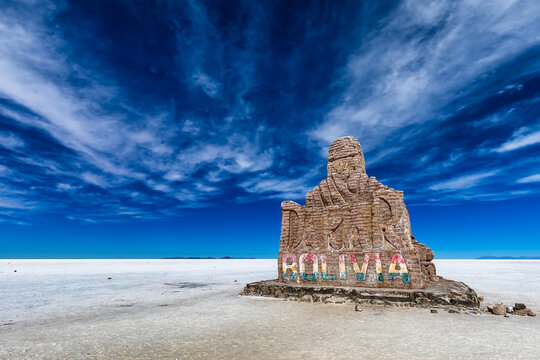 View of a weathered stone monument etched with 'Bolivia' stands starkly against the vast, shimmering salt flats under a vibrant blue sky, Uyuni, Departamento de Potos&Atilde;&shy;, Bolivia.