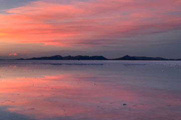 View of a serene, mirror-like expanse reflecting a vibrant pink and orange sky at dawn, with distant mountains on the horizon, Uyuni, Departamento de PotosÃ­, Bolivia.