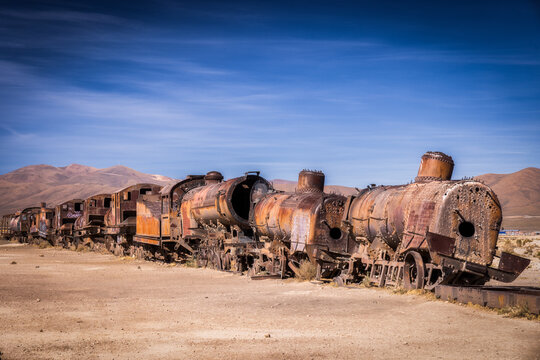 View of weathered locomotives and carriages, a skeletal train cemetery under a vast blue sky, rusting in the arid landscape, Uyuni, Departamento de Potos&Atilde;&shy;, Bolivia.
