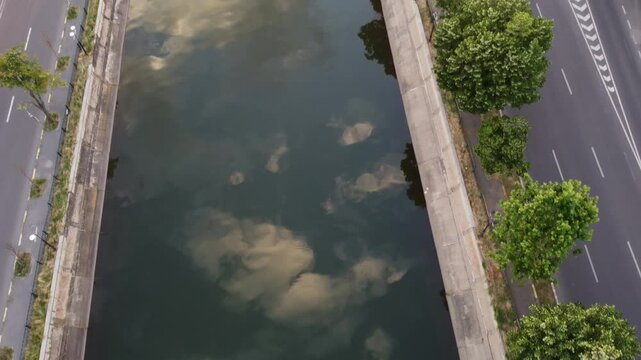 Aerial shot of the D&acirc;mbovița river in Bucharest, Romania, as the drone rises from the water&rsquo;s reflection towards the Ciurel Bridge during a warm summer sunset