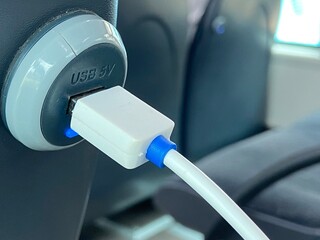 Smartphone cable connected to USB charger port in public bus transport.Mobile device charging in a...