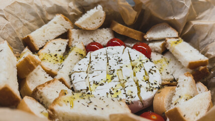 Baked camembert cheese with olive oil, herbs and cherry tomatoes served with sliced baguette bread, concept of gourmet appetizer and Mediterranean cuisine