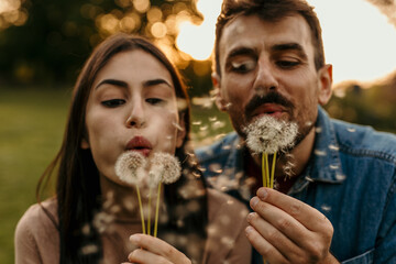Happy couple blowing dandelion seeds at sunset in nature