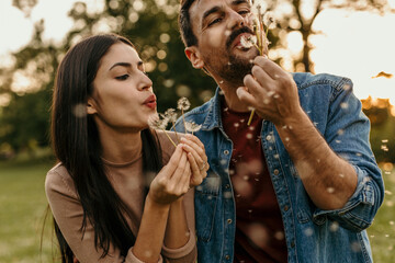 Happy couple blowing dandelion seeds enjoying a day in nature together