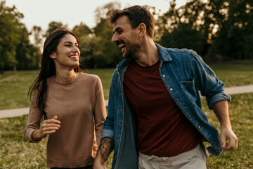 Happy couple holding hands and running through park at sunset