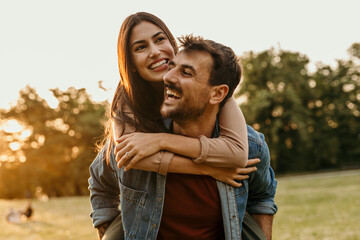 Happy couple enjoying piggyback ride in golden hour sunlight at park