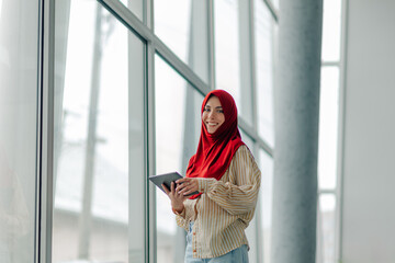 Smiling muslim businesswoman holding tablet by office window