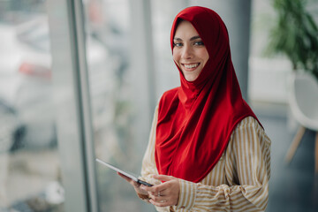 Smiling muslim businesswoman wearing red hijab using tablet in office