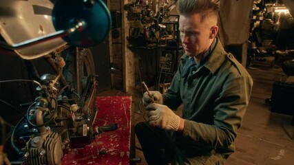 Young man in green jacket meticulously using wrench to repair motorcycle engine in dimly lit workshop - Powered by Adobe