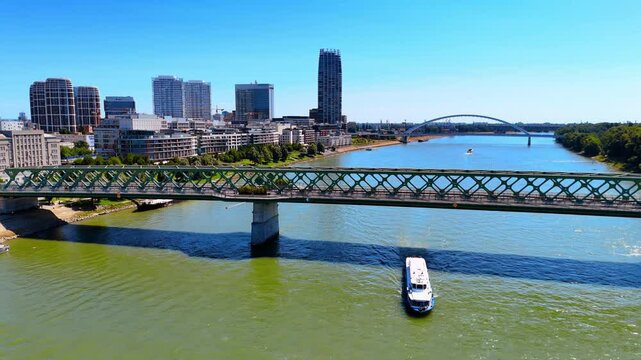 Riverboat floats under the bridge by the Danube River. Modern architecture of Bratislava, Slovakia at backdrop. Aerial view.