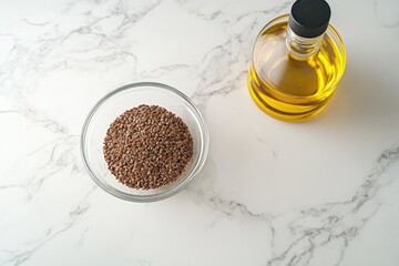 Overhead view of flax seeds in a bowl and a bottle of flaxseed oil on a marble countertop.