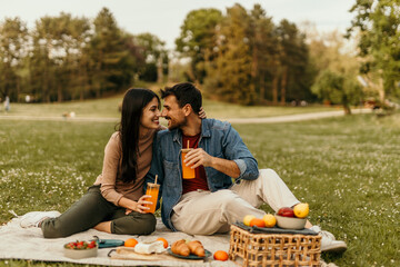 Happy couple enjoying romantic picnic in park with juice and food