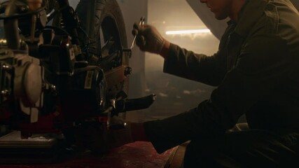 Professional mechanic meticulously working on rear wheel of vintage motorcycle using wrench in dimly lit workshop
