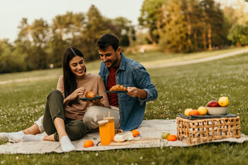 Happy couple enjoying a romantic picnic with croissants and fruit in the park