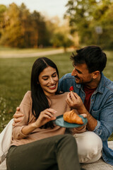 Couple sharing romantic picnic with strawberries and croissant in park