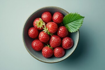 A bowl overflowing with fresh, vibrant red strawberries, complemented by a single, crisp green leaf for a natural touch.