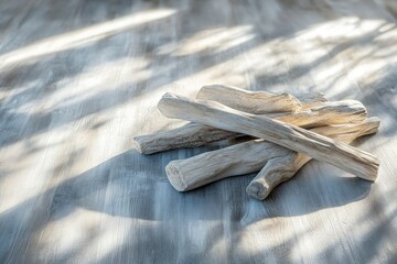 A pile of weathered driftwood rests on a gray, textured surface with soft, filtered light casting shadows.