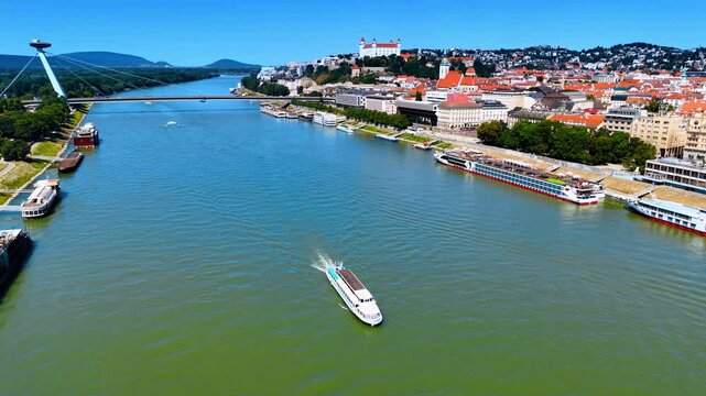 Large riverboat floats by the waterscape of the Danube River in Bratislava, Slovakia. Aerial perspective on the old city with orange-roofed buildings.