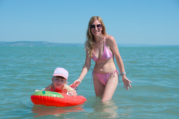 girl swims on inflatable toy accompanied by mother