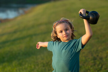 Child lifting the kettlebell in backyard outside. Cute little boy doing exercises with dumbbells. Portrait of sporty child with dumbbells. Happy child boy exercising. Healthy activities kids.