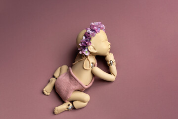 Newborn doll on pink background with flower wreath