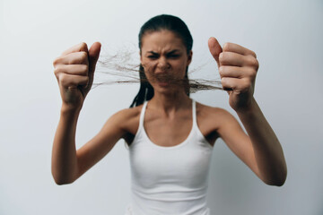 frustrated woman pulling her hair with a pained expression, wearing a white tank top, against a...