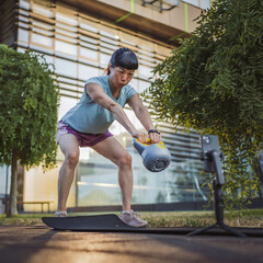 Japanese mature woman filming a workout video with kettle bell weight