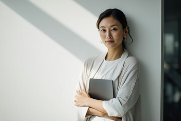 Confident young Asian woman standing indoors holding a tablet, looking at camera with a calm and professional expression