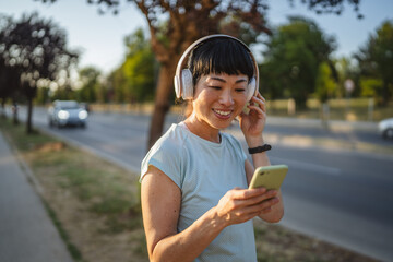 Smiling japanese woman use cellphone while jogging on the street
