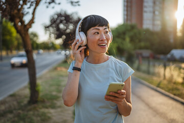 Smiling japanese woman use cellphone while jogging on the street