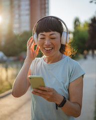 Smiling japanese woman use cellphone while jogging on the street