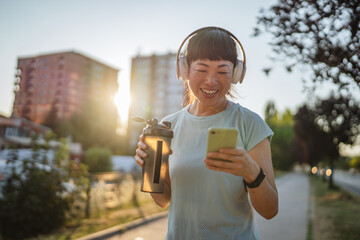 japanese woman drink protein shake and use mobile phone after jogging