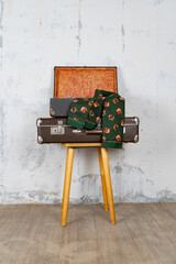 Vintage retro suitcase, the suitcase is open and there is a scarf in it, stand on a stool. The background is a white wall. The concept of retro travel and retro design.