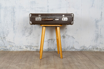 Vintage suitcase stand on a stool against a white wall. The concept of retro travel and retro design.