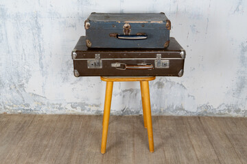 Two vintage suitcases stand on a stool against a white wall. The concept of retro travel and retro design.